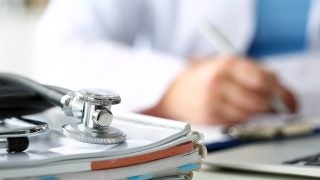 A stethoscope lies on a stack of notebooks and books
