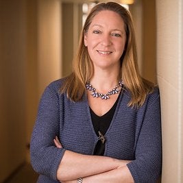 A headshot of Lynn Overmann, the new executive director of the Beeck Center at Georgetown. In this picture, Lynn is smiling at the camera and folding her arms across her chest. She is wearing a blue sweater and a silver necklace.