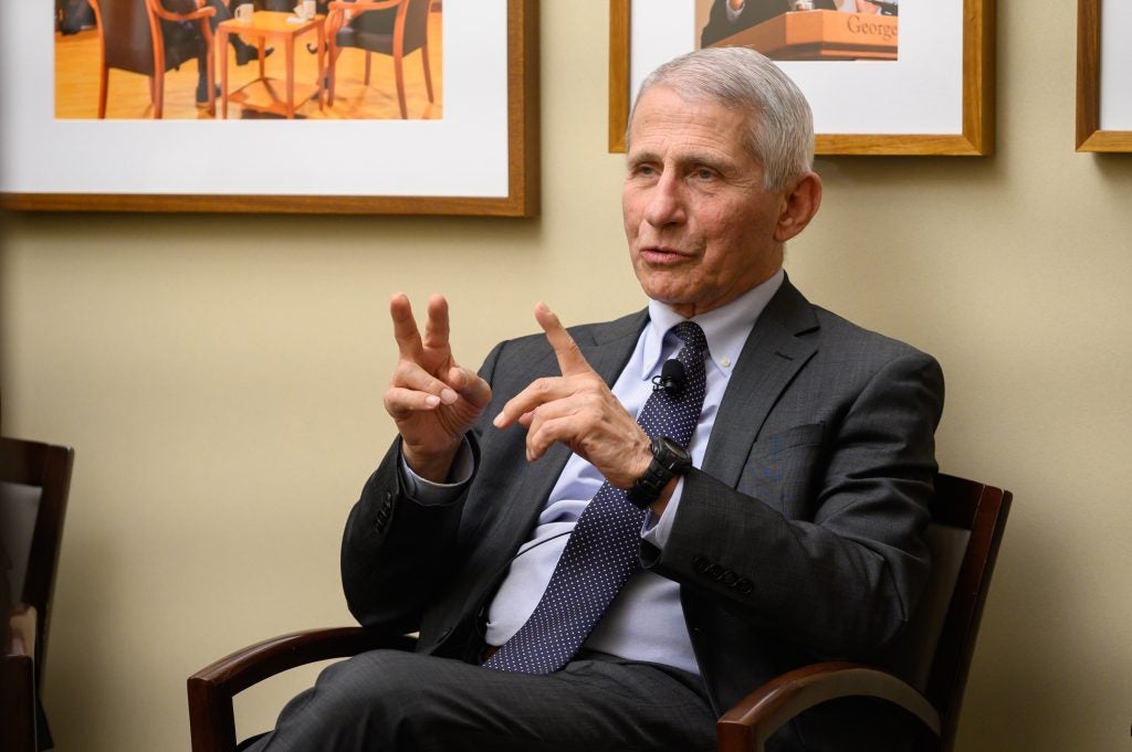 Dr. Anthony Fauci sits in a chair at Georgetown. He is wearing a suit and gestures with his hands as he talks.