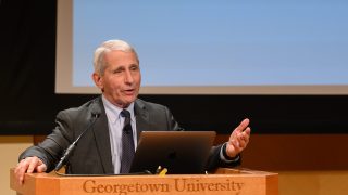 Dr. Anthony Fauci delivers a presentation at a podium in the Lohrfink Auditorium