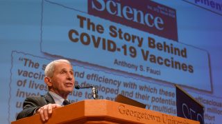 Dr. Fauci speaks from behind a podium at Georgetown University. Behind him is a screen of an article from Science magazine that says, &quot;The Story Behind COVID-19 Vaccines.&quot;