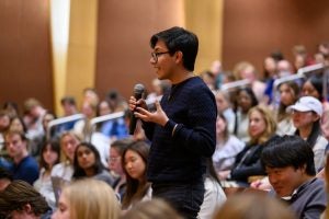 Ulises Olea Tapia (SFS‘25), a sophomore studying international politics, stands up during Dr. Fauci's talk to ask a question. He is holding a microphone and wears glasses.