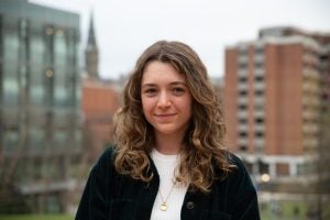 Ursula Gately (C’23), a senior who’s majoring in biology of global health, slightly smiles at the camera after Dr. Fauci's talk. She stands outside on Georgetown's campus with buildings behind her. 