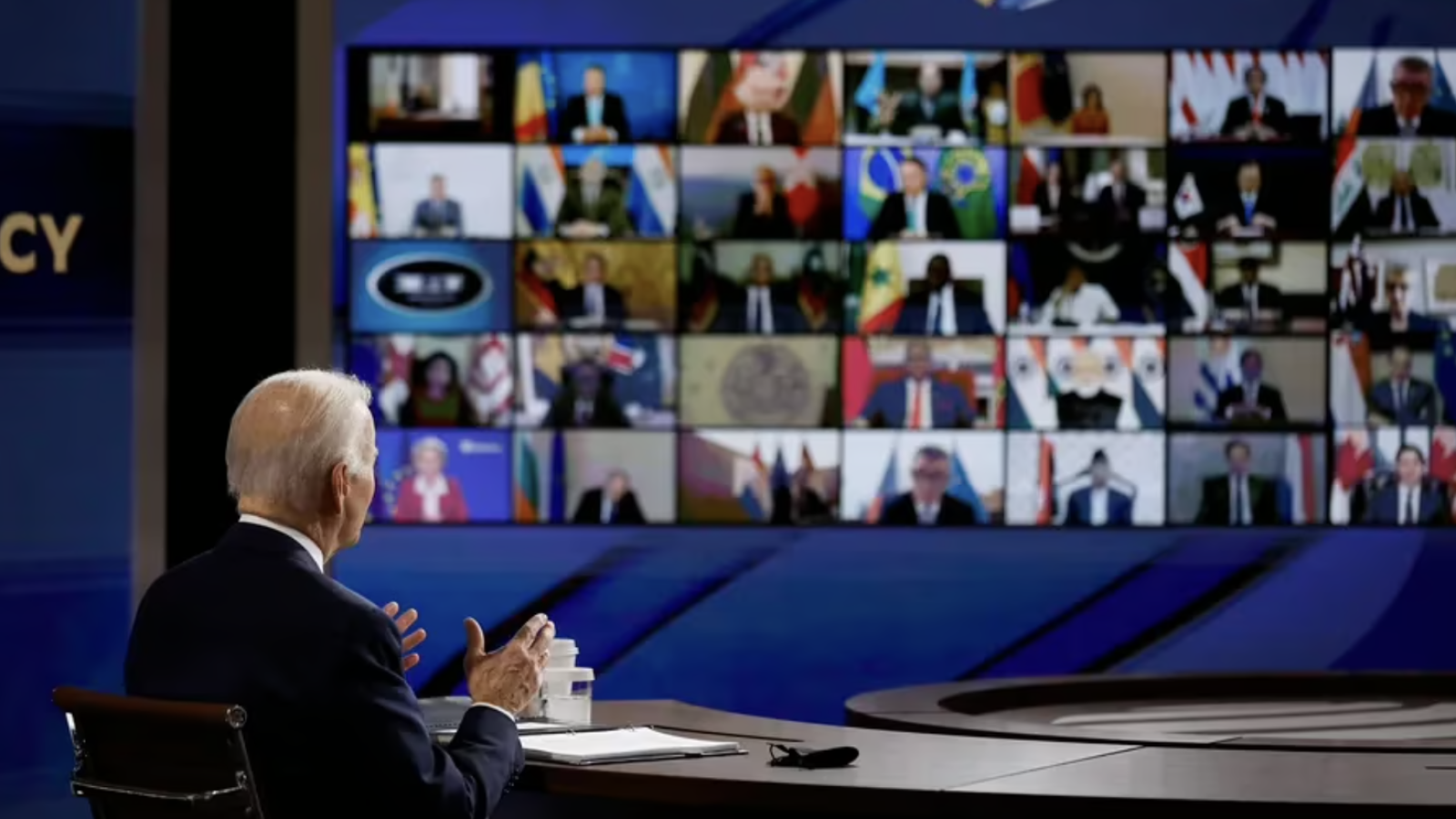 Biden, speaking to a zoom audience with monitor in background.