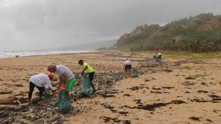 A group of volunteers on Barbados remove trash from the beach on a cloudy day.