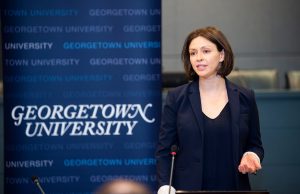 Georgetown researcher Katie Wells presents to an audience in front of a blue standing poster that says "Georgetown University."