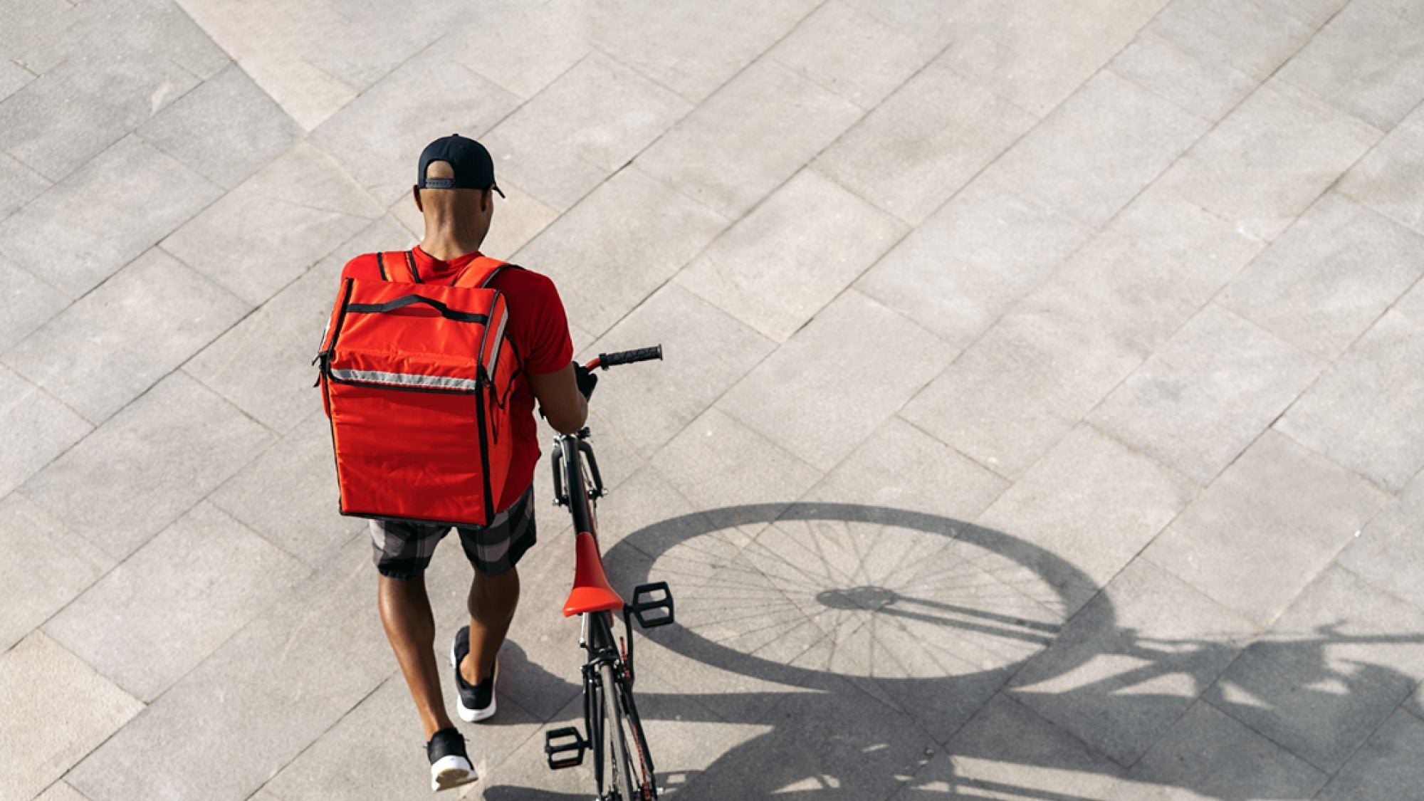 Aerial shot of a food delivery worker, who is wearing a backpack and pushing a bike