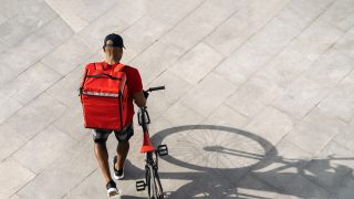 Aerial shot of a food delivery worker, who is wearing a backpack and pushing a bike