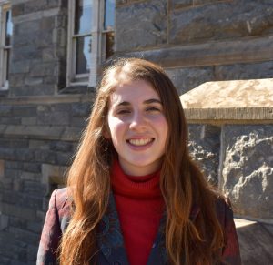 Isabella Stratta (SFS'25) helped research employment practices for instant food delivery platforms for a new Georgetown report. In this image, she stands outside Healy Hall smiling at the camera. She wears a red turtleneck and blazer.