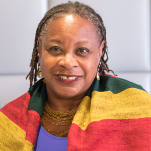 A headshot of Anita Gonzalez, a professor of performing arts and African American studies. Anita wears a bright red, yellow and green scarf, a purple shirt and a gold necklace.