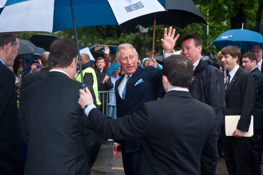 Under an umbrella, King Charles waves to the crowd
