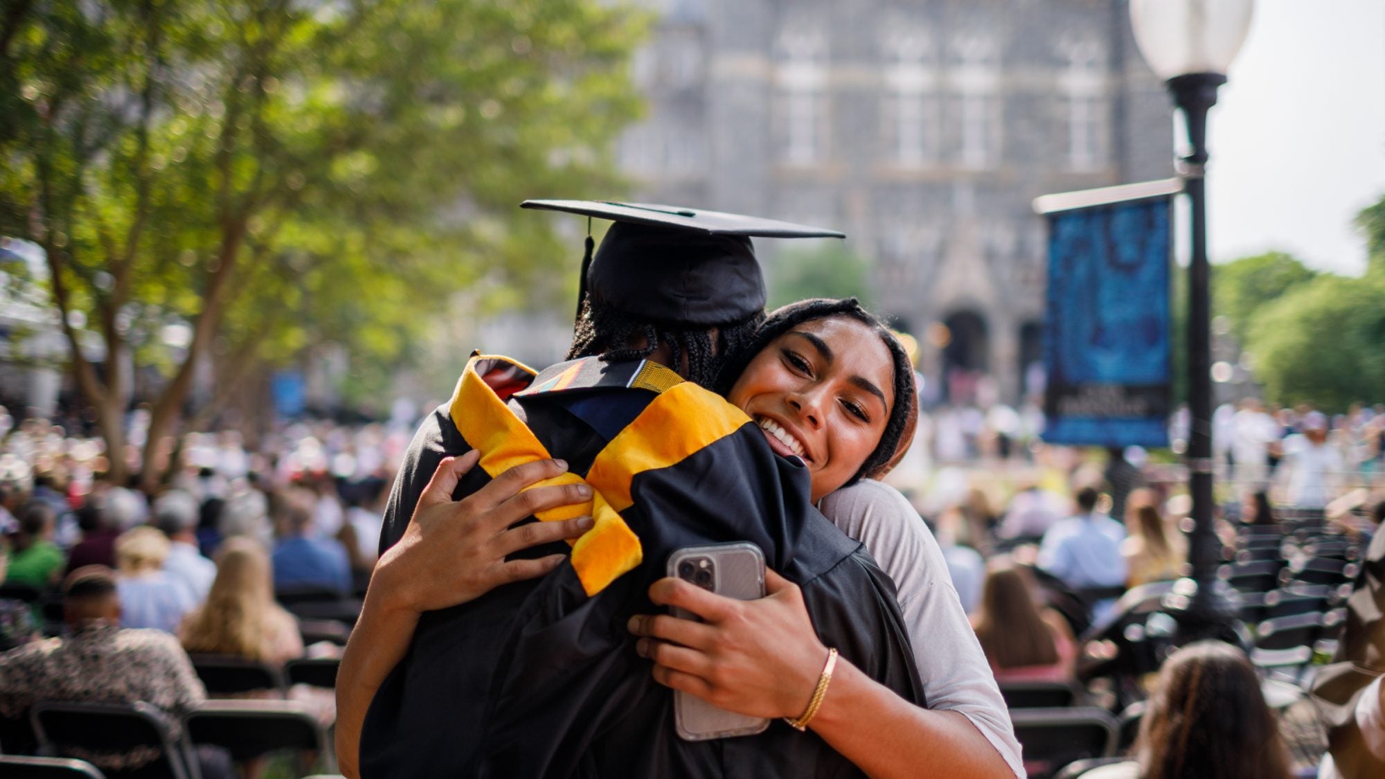 A family member hugs a Georgetown graduate. You can see the face of the person hugging the graduate, and she is smiling while looking at the camera