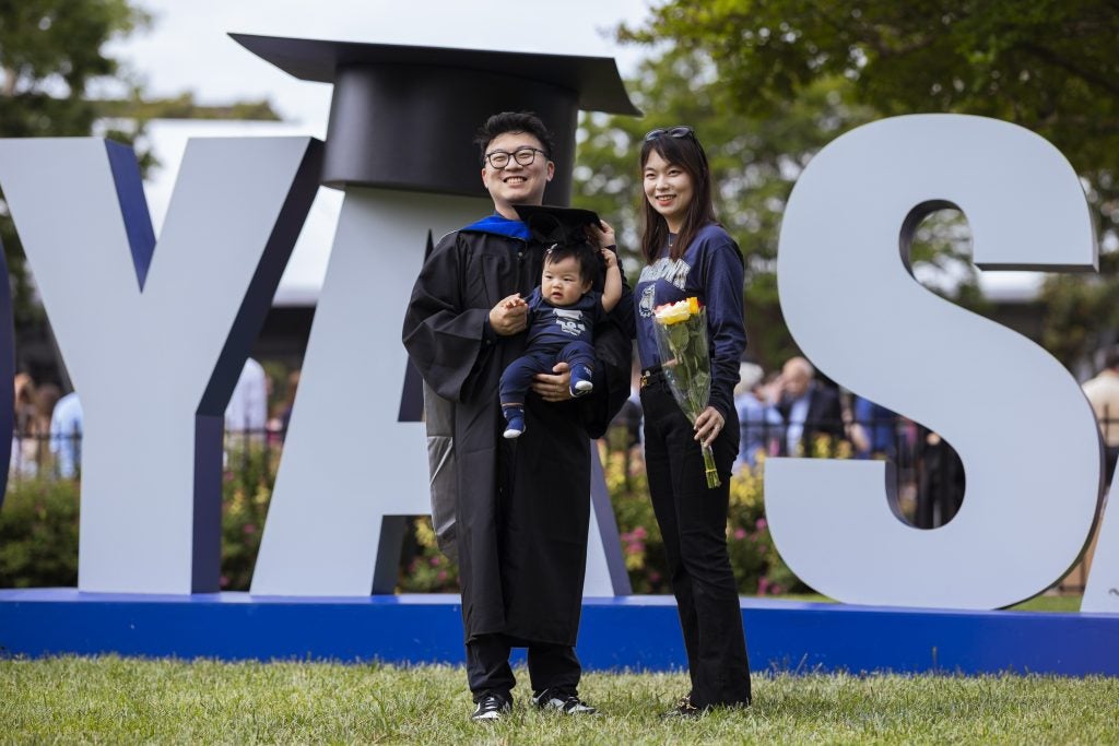 A man and woman in graduation robes with a baby boy