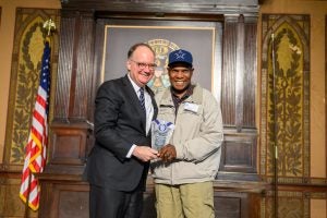 President John J. DeGioia stands on stage with John Matthews holding his service award in Gaston Hall.