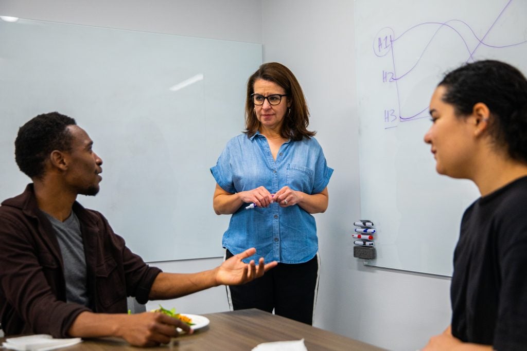 Gandawa speaks while his professor and a classmate listen in front of a white board.