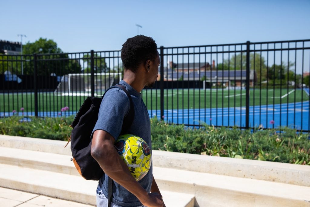 Gandawa walks outside of a gated soccer field.