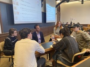 Cassera sits in a classroom in discussion with five others around a table.