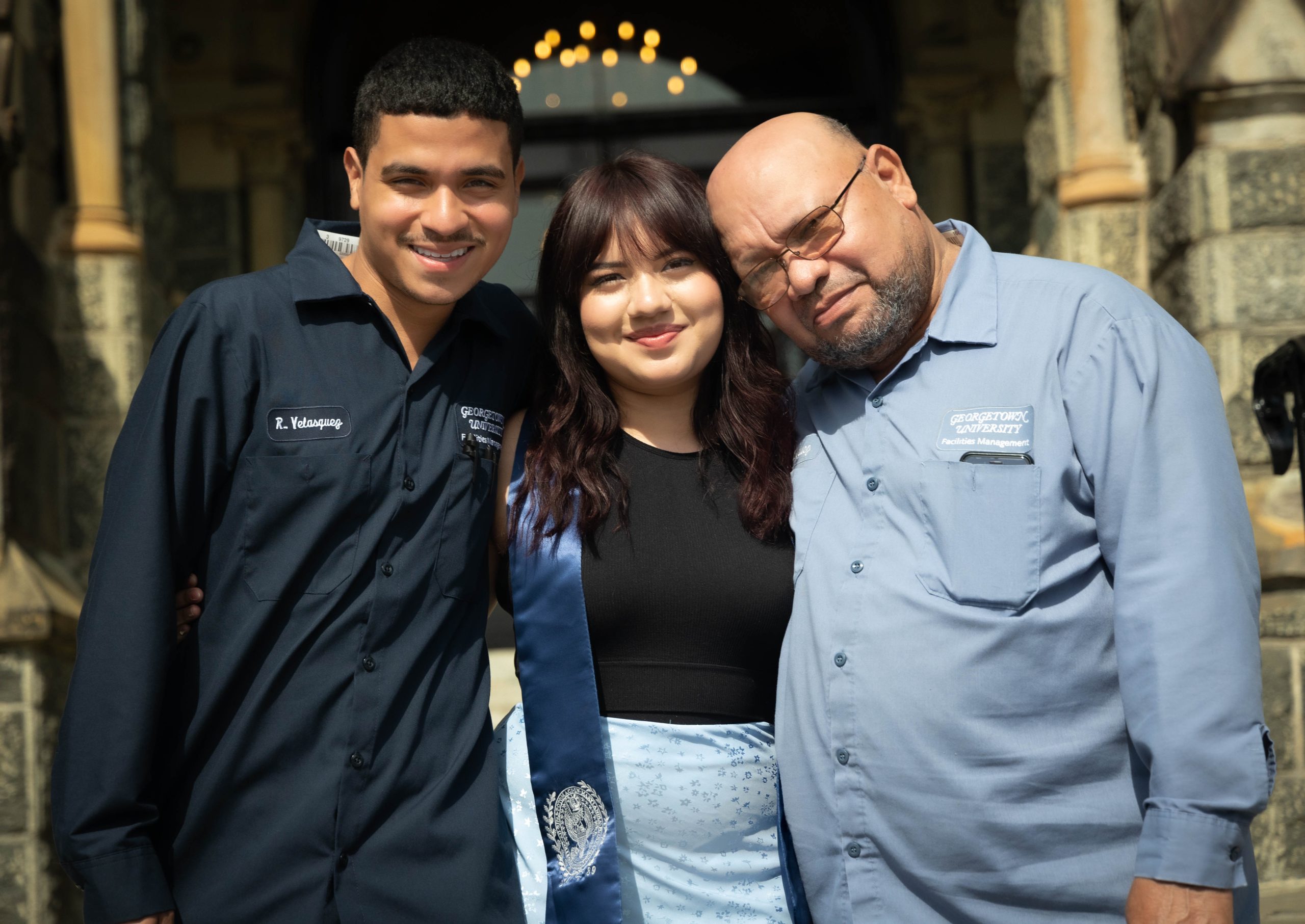 The Velasquez family stands on the front steps of Healy Hall posing for a picture. Reynaldo (left), Gaby (center) and Francisco (right) smile at the camera.
