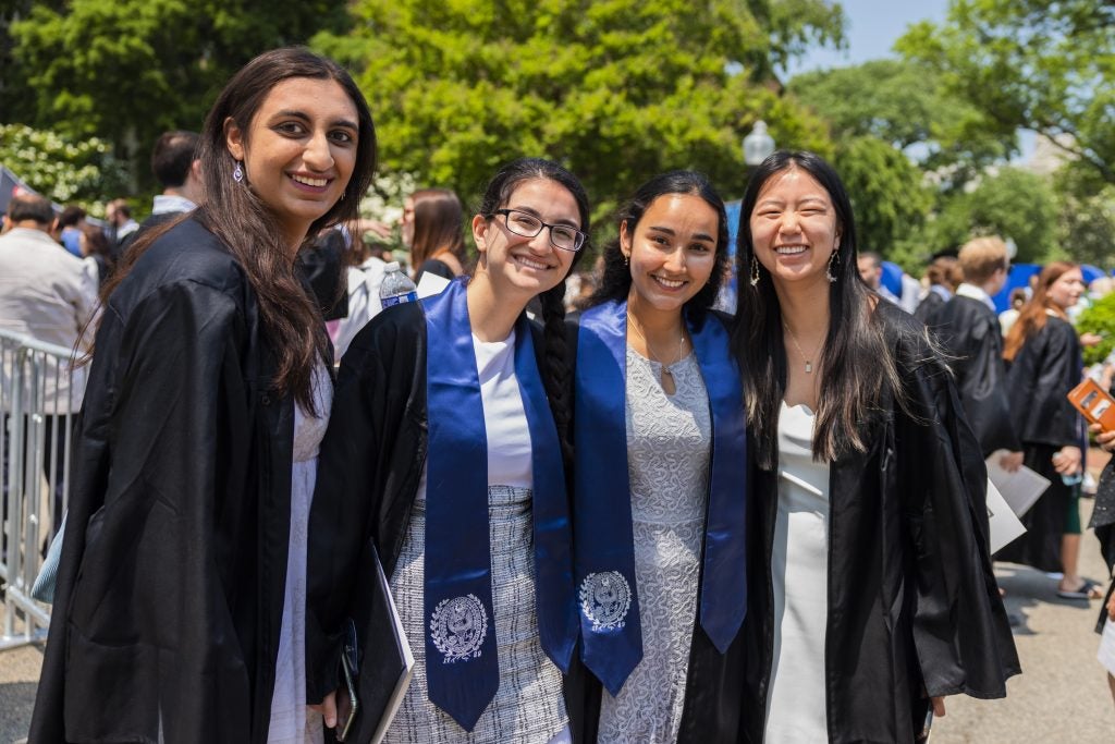 Four Georgetown graduates in black robes pose for a photo together at commencement