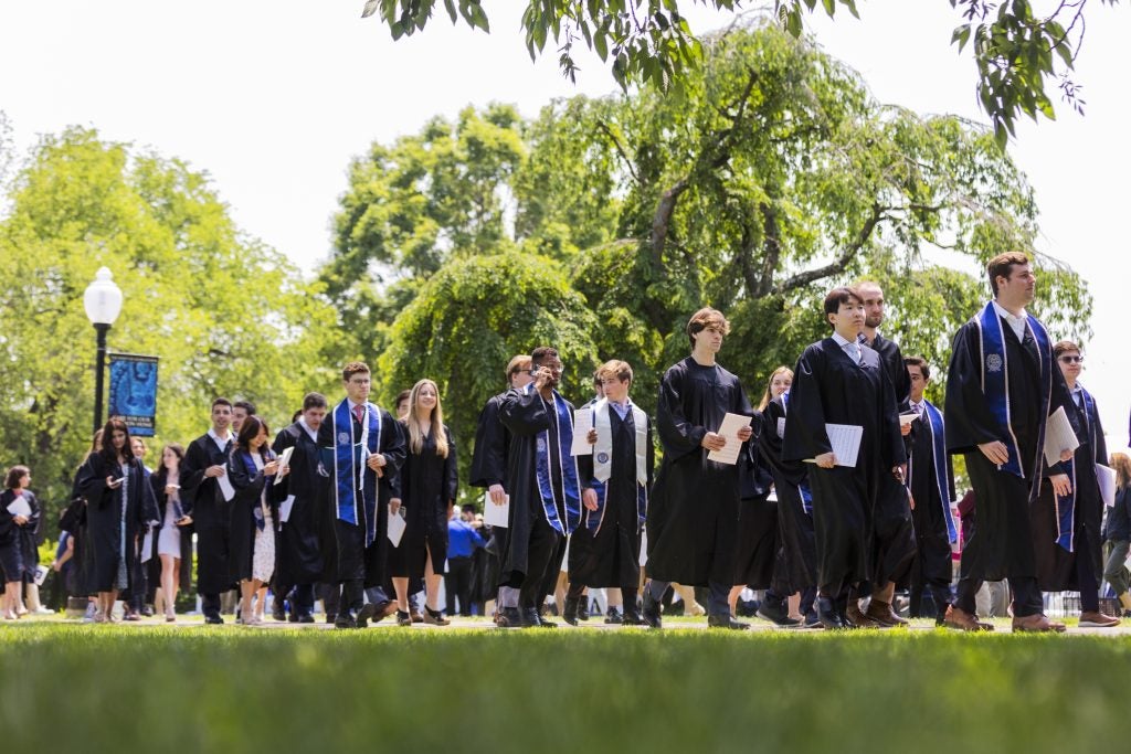 Graduates in black robes walk down Copley Lawn during procession