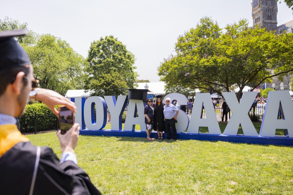 A Georgetown graduate and two other people pose for a photo in front of the giant letters on Copley Lawn that spell out "Hoya Saxa"