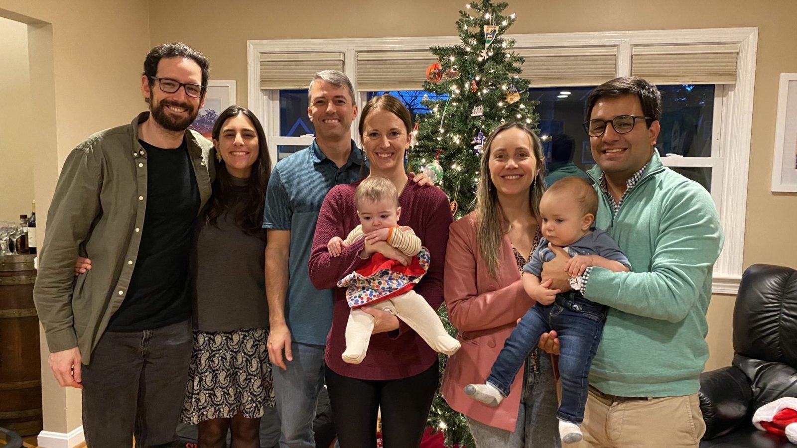 A group of student-parents and their babies in a home with a Christmas tree.