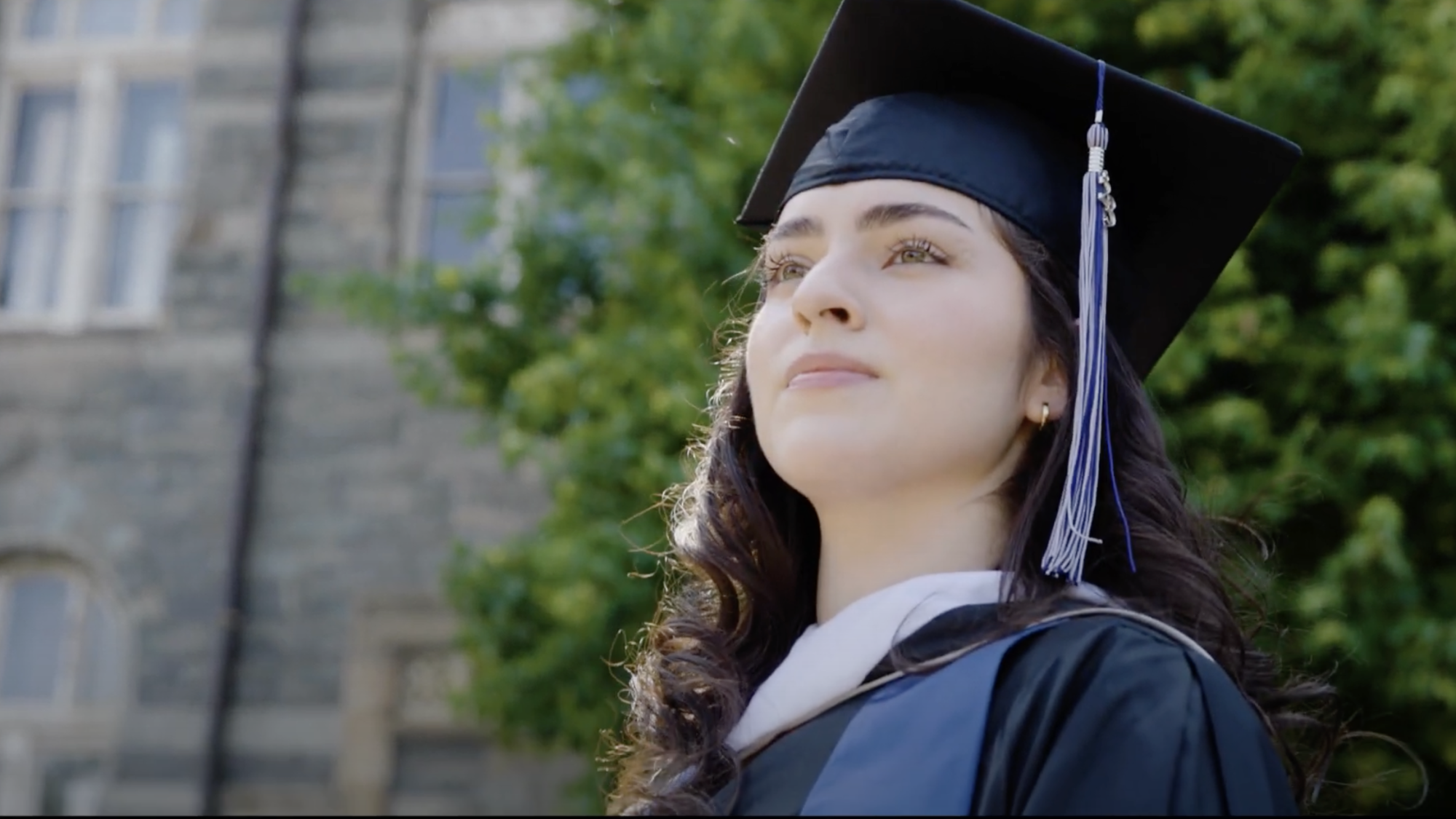 A Georgetown graduate in regalia looks knowingly into the distance while standing at the bottom of the steps of Healy Hall