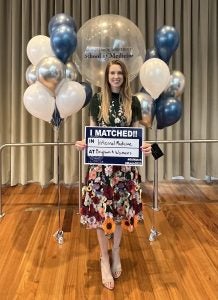 Fitzgerald standing in front of balloons holding a sign showing where she matched for her residency.