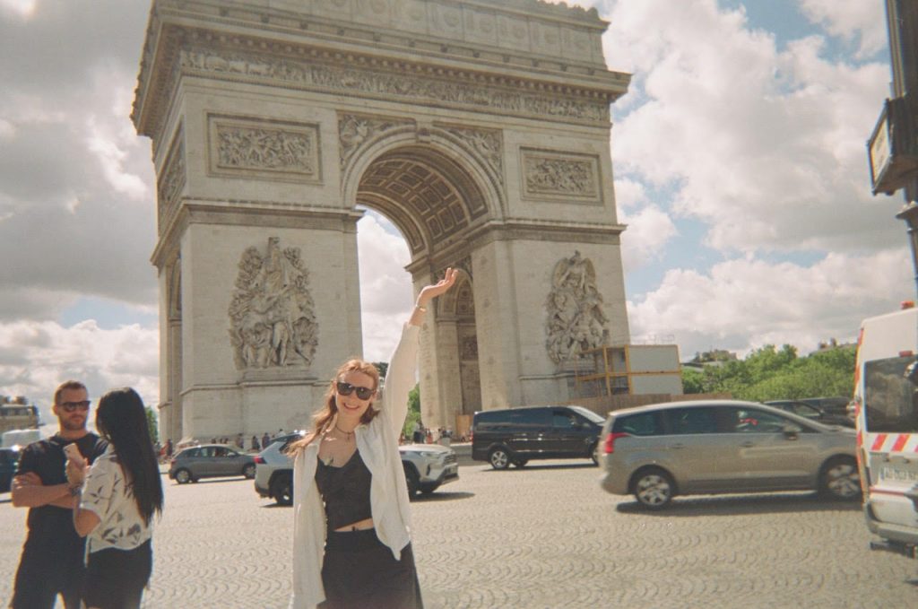 Hardy stands with the Arc de Triomphe behind her as cars pass through the roundabout.