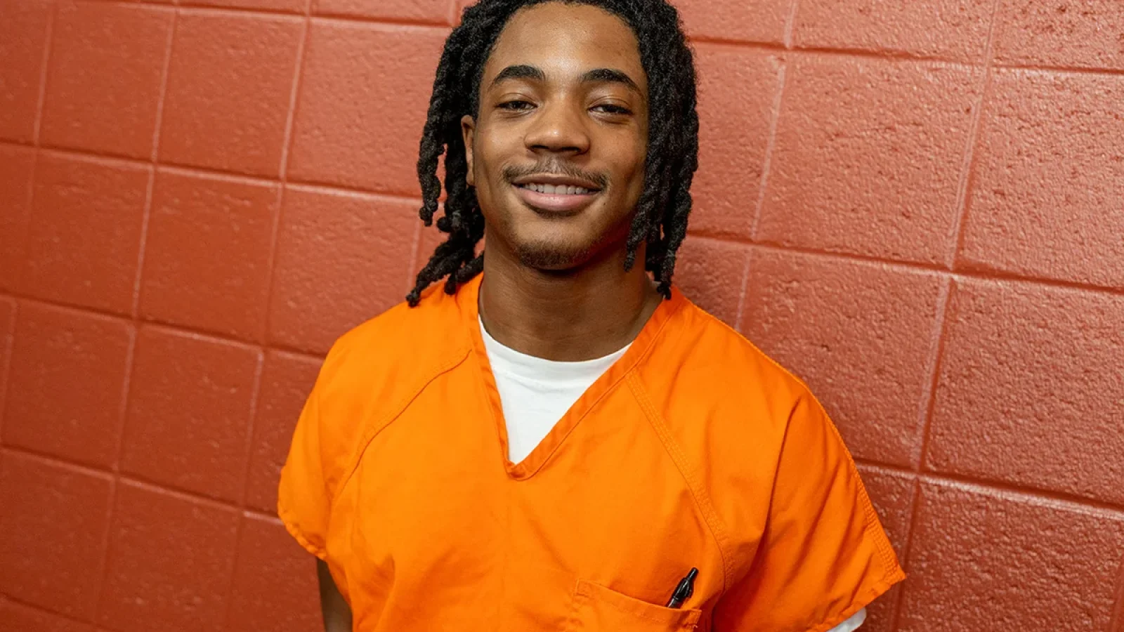 Georgetown Prison Scholar Keonte Lewis wears an orange jumpsuit in the DC jail, smiling at the camera.