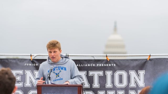 Jackson Mittleman (C'23) speaks at a rally for gun violence prevention. Behind him is a sign that says "Generation Lockdown" and the U.S. Capitol is in the foreground.