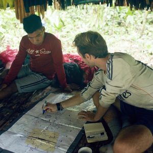 Brian Griffiths talks to a Maijuna guide while pointing toward a map on the ground.