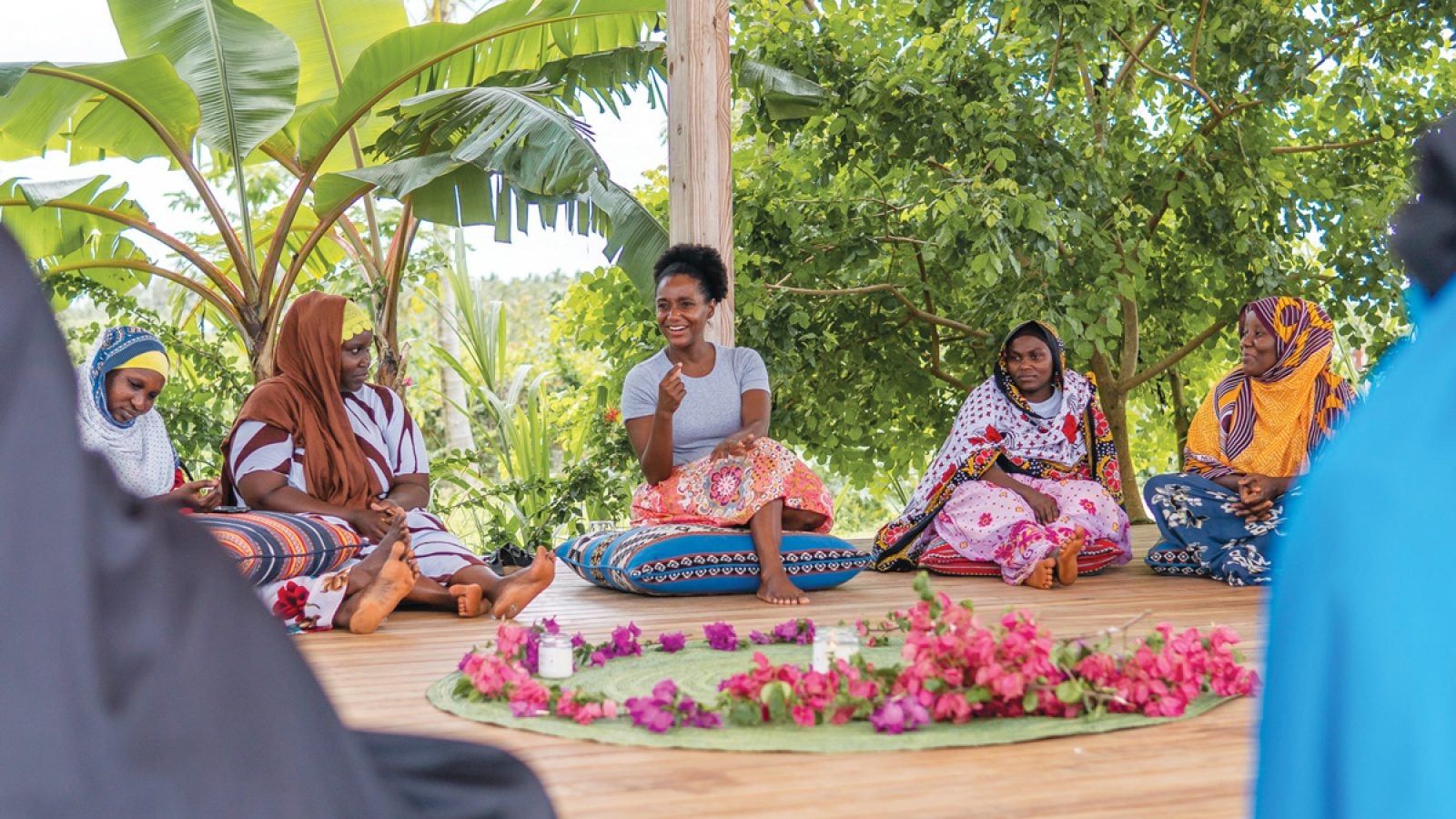 Certified nurse midwife Nafisa Jiddawi(NHS&#039;14) sits on a pillow on the ground of a holistic wellness center dedicated to women&#039;s health promotion and disease prevention that she established in Tanzania. In front of her lays a circle of flowers; behind her are palm fronds.