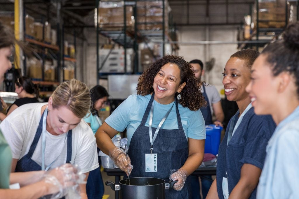 A group of women smile and talk as they prepare food to serve at the soup kitchen.