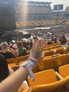 A hand adorned with friendship bracelets outstretched toward a stadium