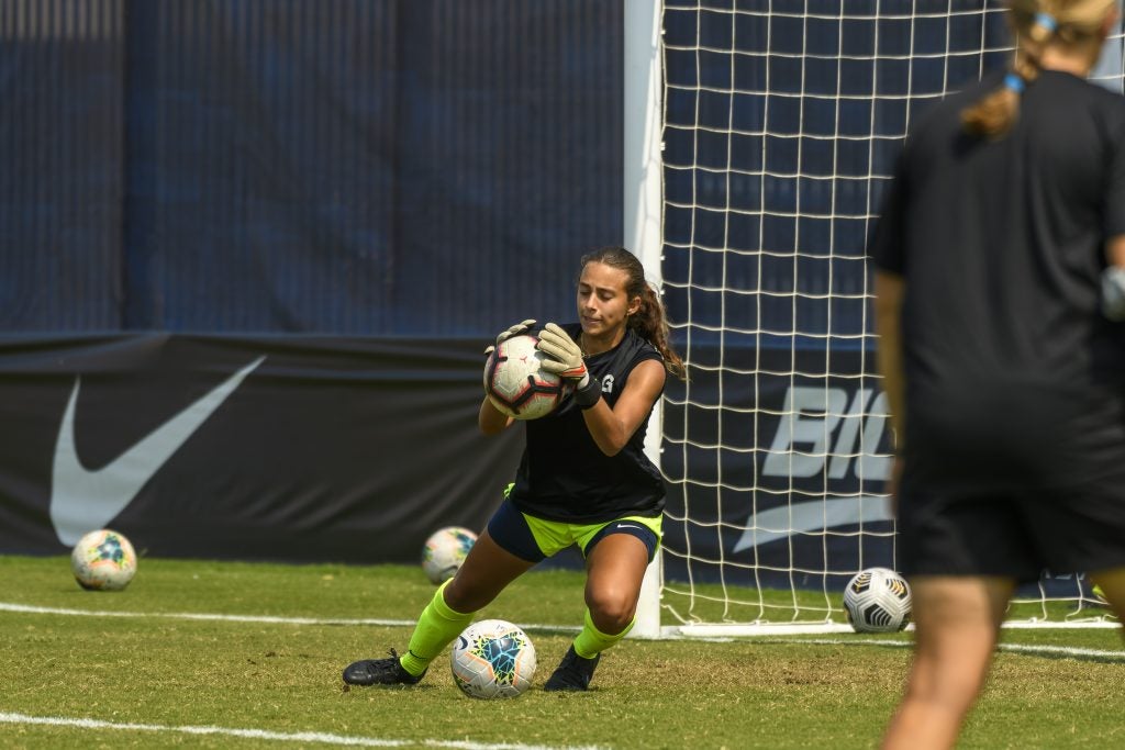 Lara Larco (C'15) catches a soccer ball in front of a goalpost on a soccer field.