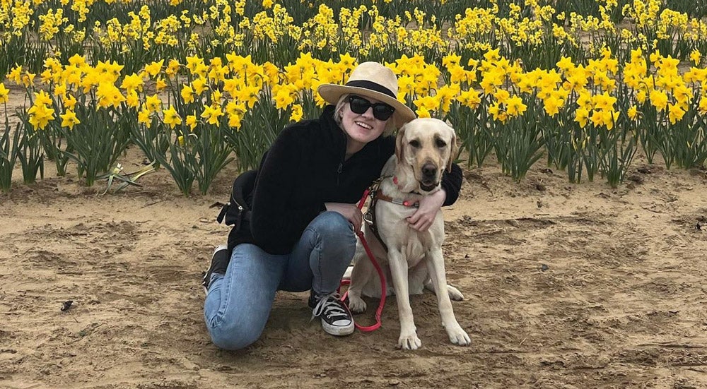 Marissa Nissley (B'24) kneels and smiles with her guide dog, Smalls, a golden retriever.