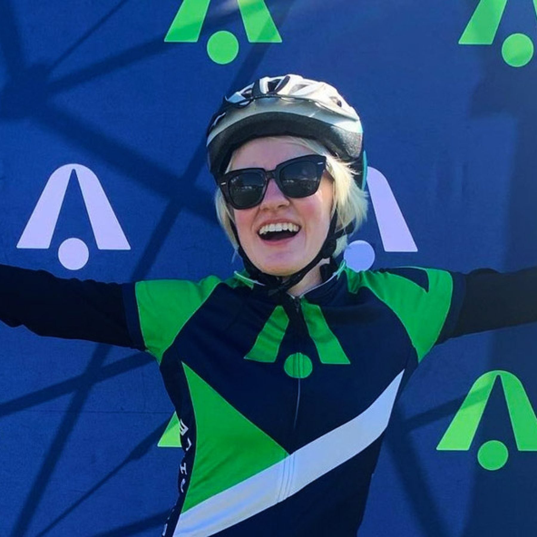 Marissa Nissley (B&#039;24) stands at the finish line after a 50-mile race with her arms outstretched. She wears black sunglasses and a helmet.