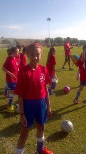 Lara Larco (C'15) pictured at a young age posing for a picture in a red jersey on the soccer field.