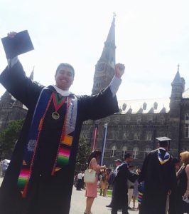 Gonzalez, on his graduation day from the Georgetown College of Arts & Sciences in May 2015, dressed in a graduation gown holds his hands up cheering.
