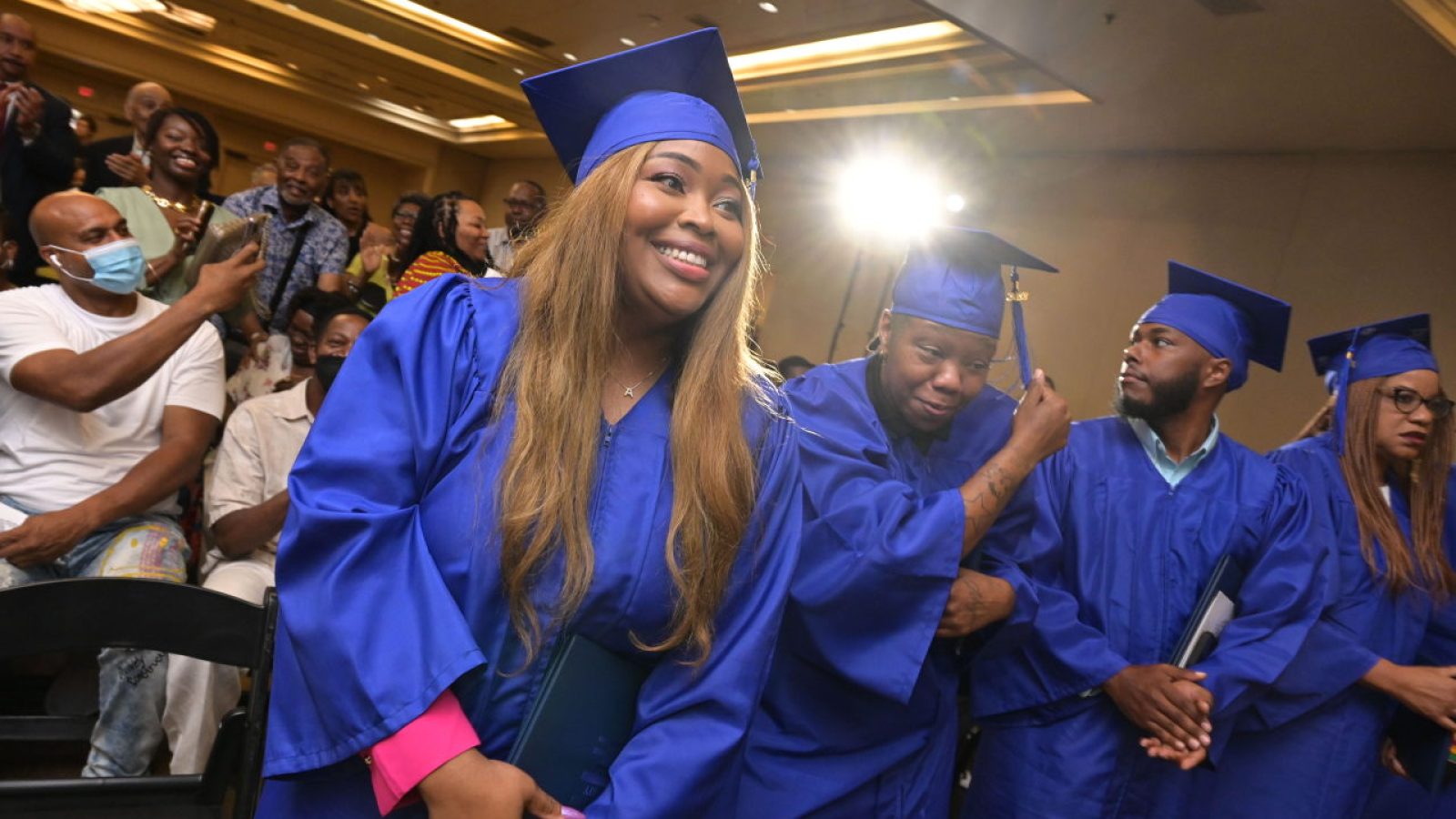 A female graduate of the Pivot Program wearing a blue cap and gown smiles as she graduates.