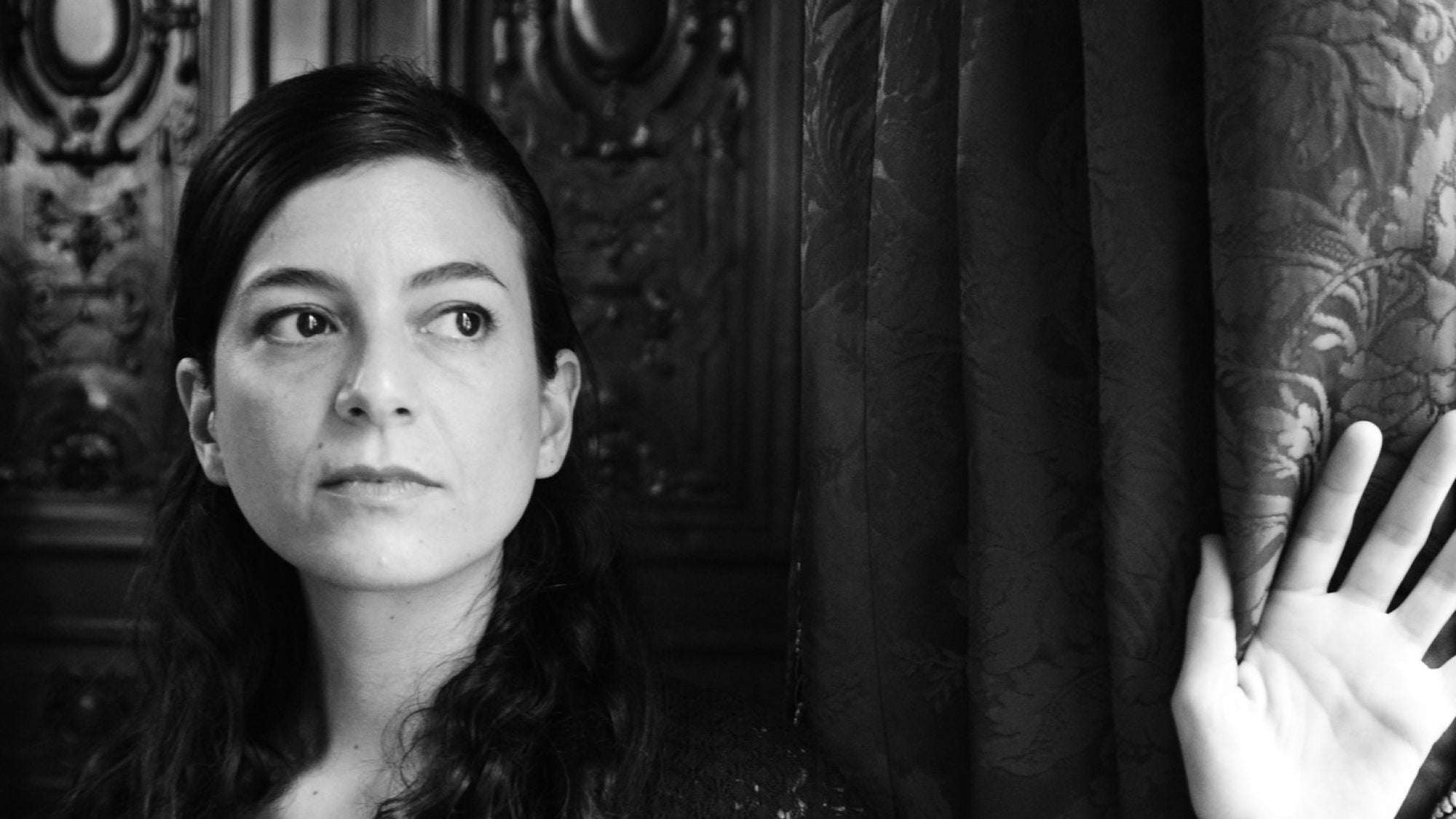 Samanta Schweblin facing camera with hand raised, black and white.
