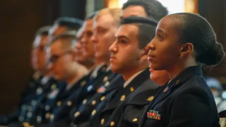 A group of men and women dressed in military apparel look forward.