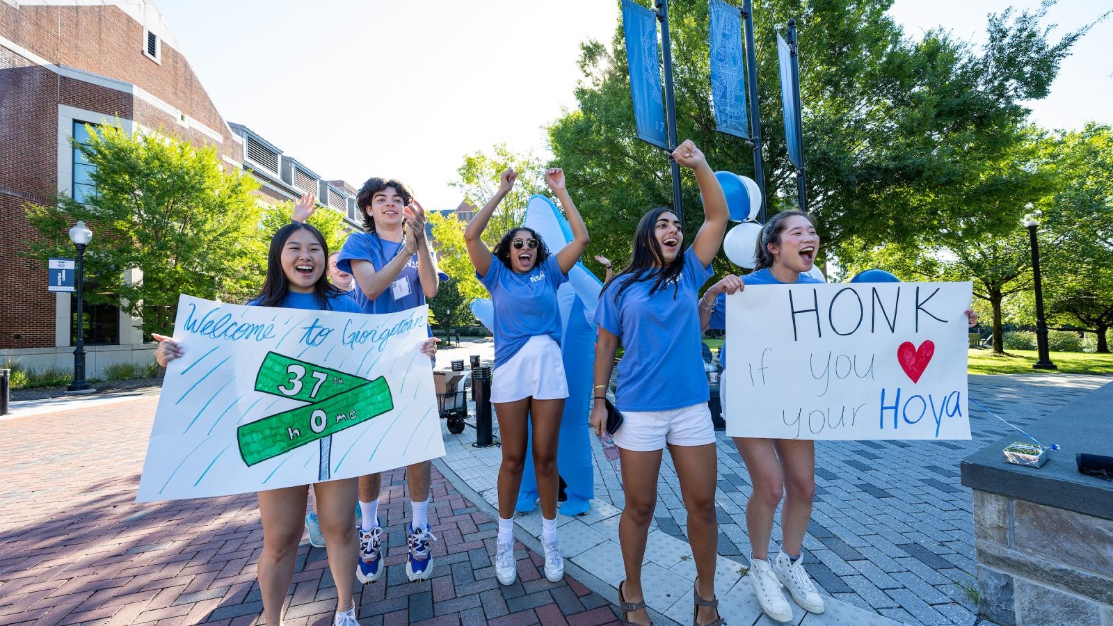 Students in blue T-shirts cheer on new students while holding up welcome signs