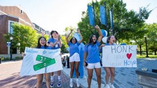 Students in blue T-shirts cheer on new students while holding up welcome signs