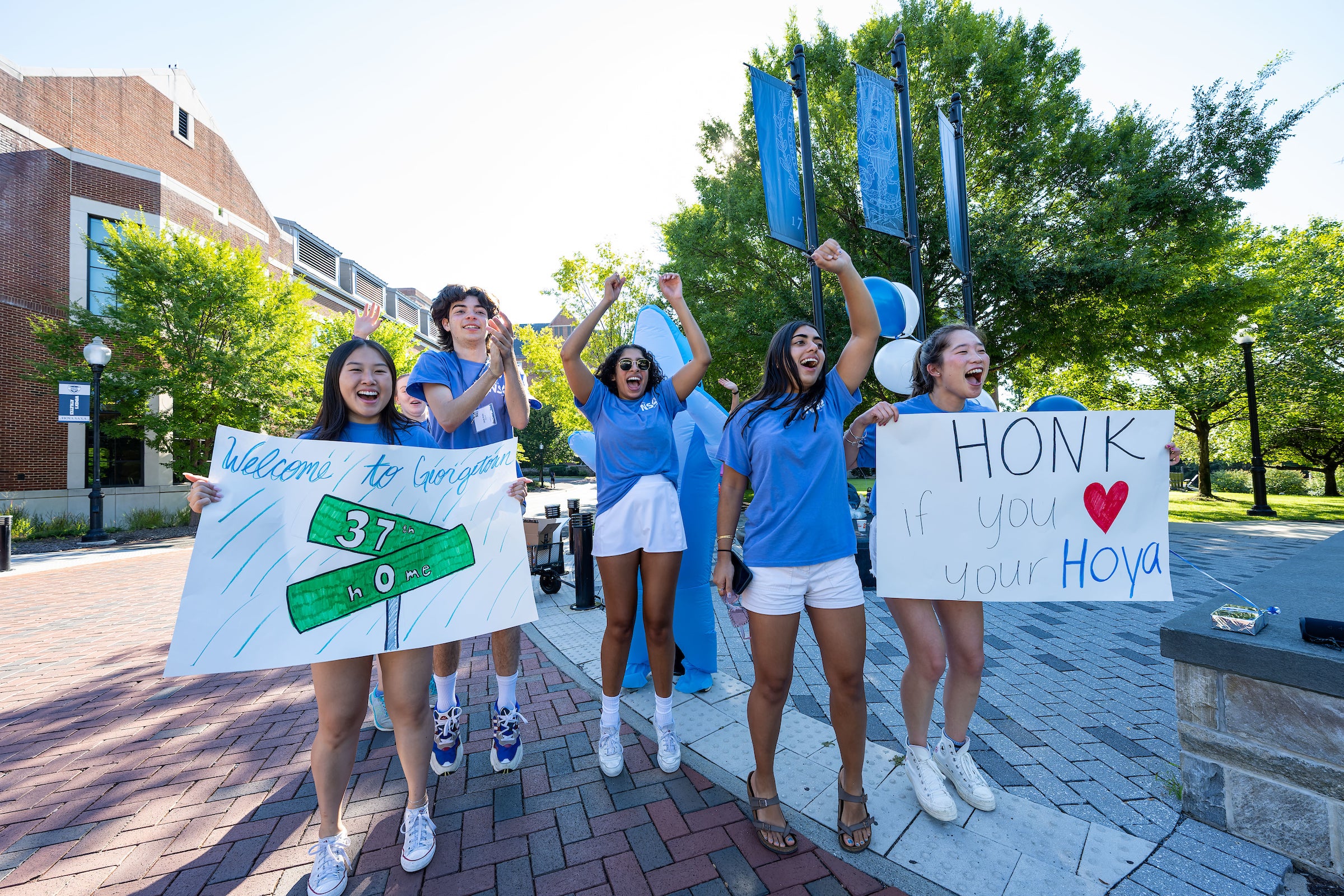 Students in blue T-shirts cheer on new students while holding up welcome signs