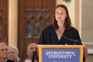 Naomi Greenberg (C’24) wears a black gown and stands before students at convocation during her speech.