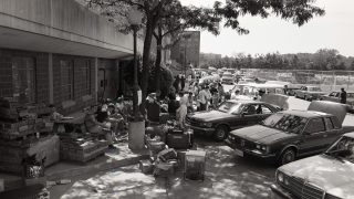 Black and white photo of cars by Harbin Hall with suitcases outside