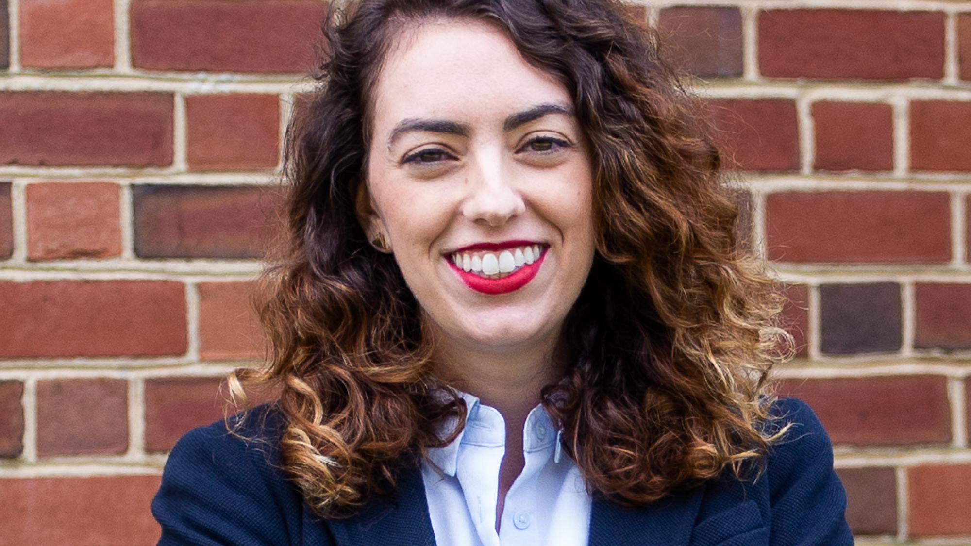 Rachel Ellis in blue blazer, standing in front of brick wall.