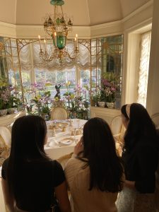 Three girls face away looking out at an ornate room with a chandelier